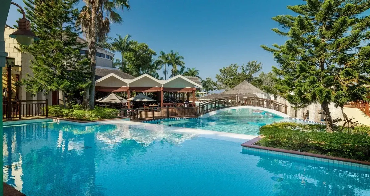Panoramic view of the resorts pool with a tiny bridge and a bar