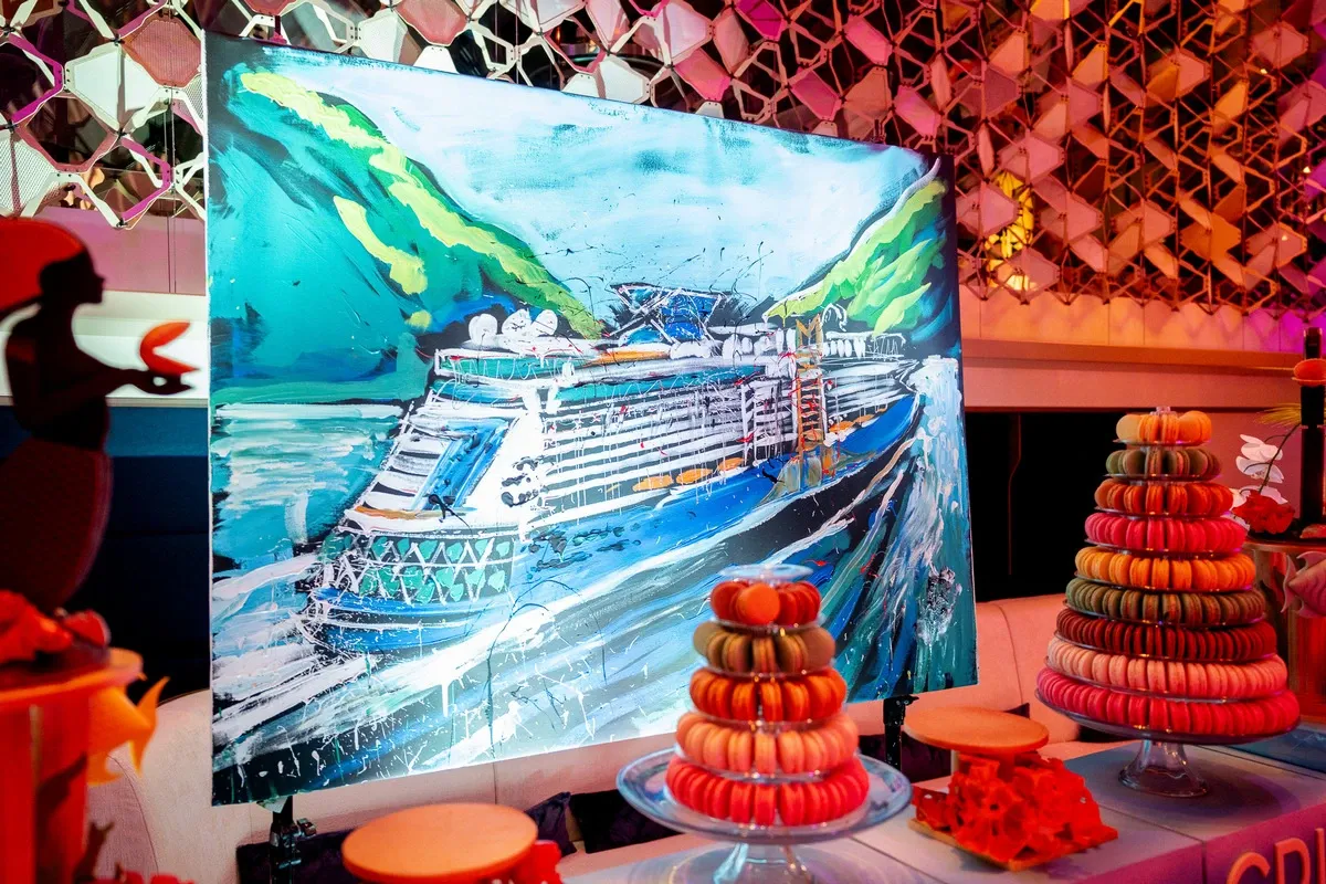 Cruise ship painting on a table next to a plate of macarons