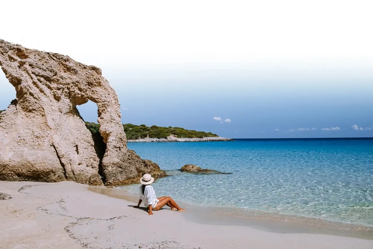 Woman sitting on a beach next to a rock