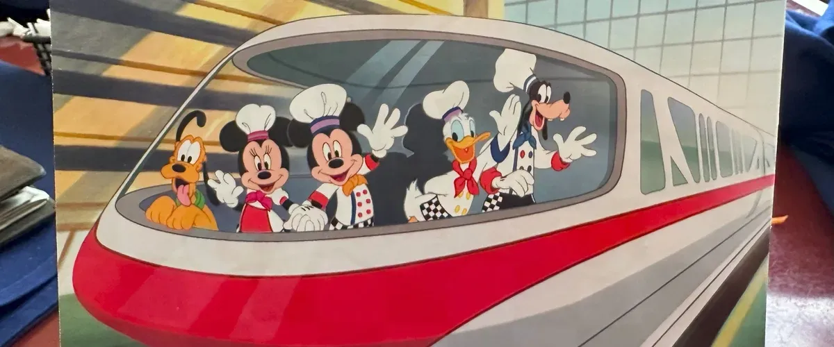 Mickey Mouse and friends, dressed as chefs, wave happily from inside a sleek, futuristic monorail with a red stripe, while Pluto looks on excitedly.