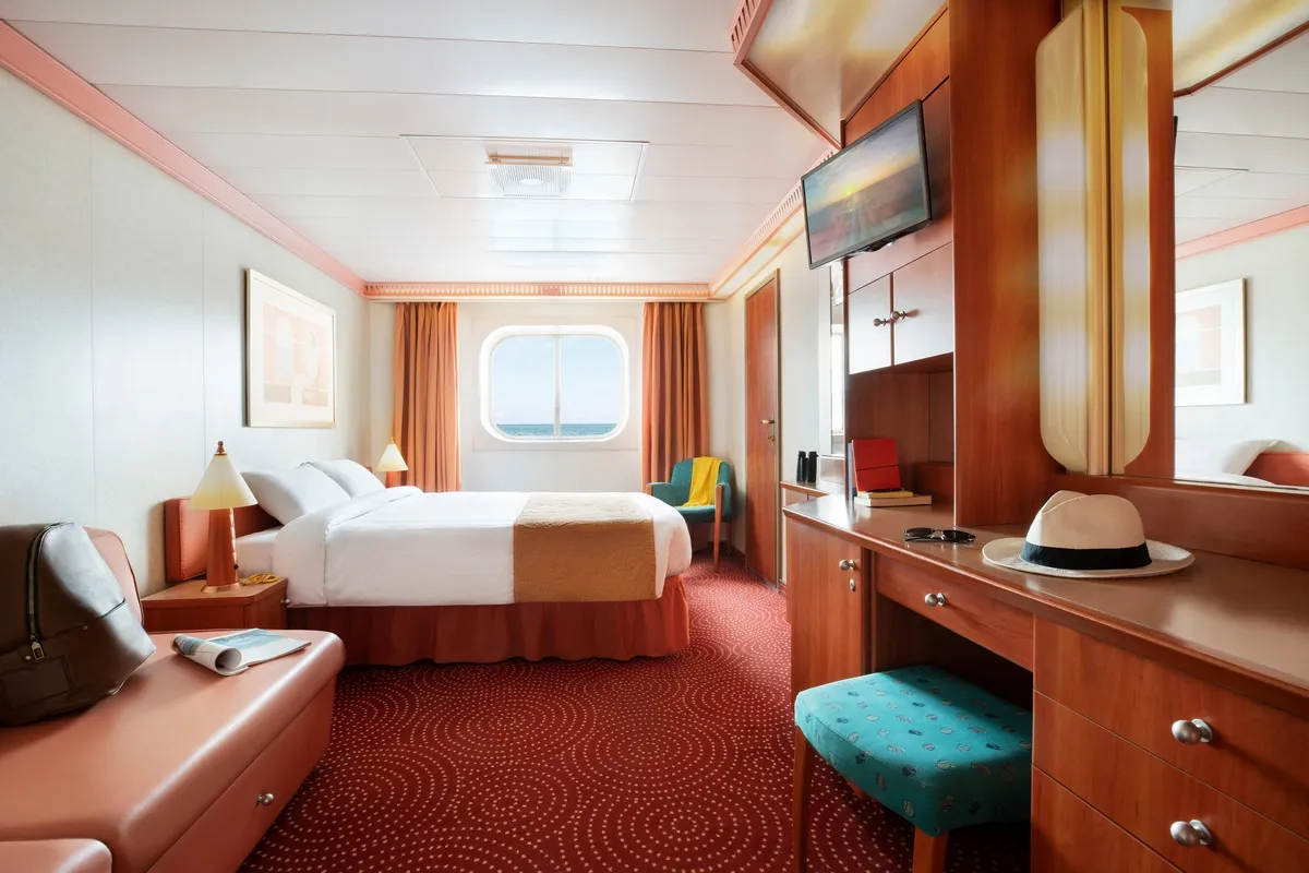 Cruise ship suite with living space, a large bed, and views to the ocean