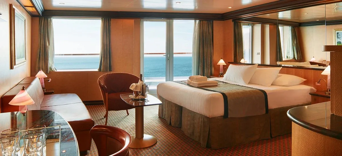 Cruise ship suite with living space, a large bed, and views to the ocean