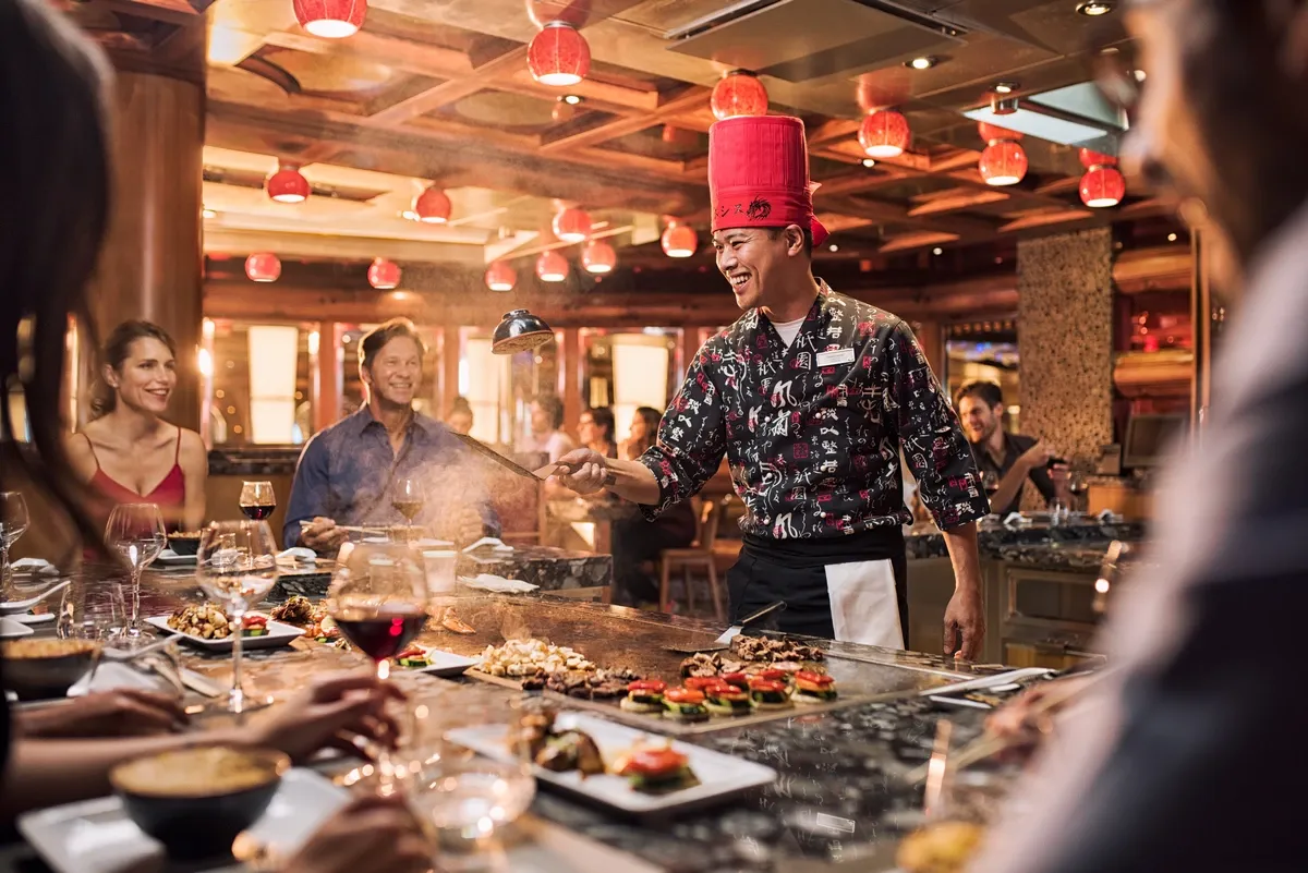 Chef cooking at an asian grill bar surrounded by people