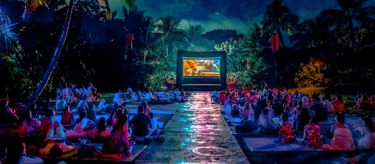 Large group of people looking at a movie on the outdoors at night
