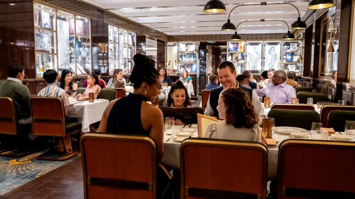 People are dining and conversing at elegantly set tables in a warmly lit restaurant, with decorative glass displays lining the walls.