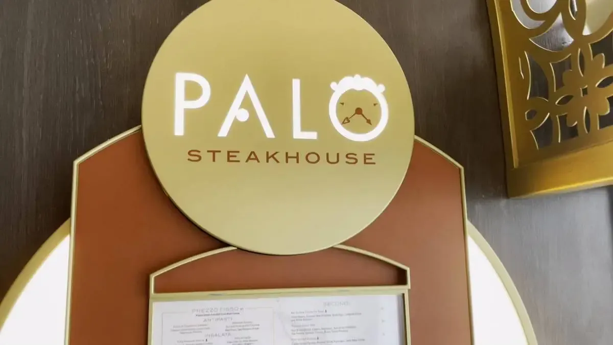 A gold sign for "Palo Steakhouse" is mounted on a wall, featuring elegant lettering and a small clock design incorporated into the letter "O.".