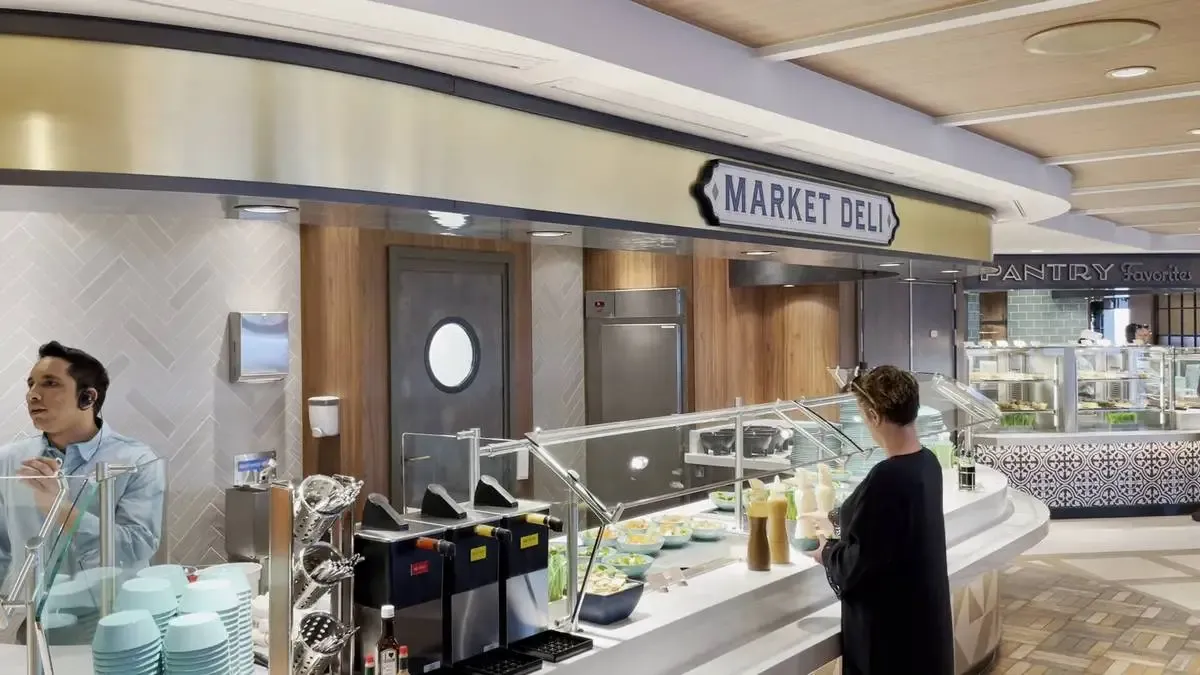 A person stands at a modern buffet counter labeled "Market Deli," selecting items from an array of dishes. The setting is bright and clean, with light wood and metal accents. In the background, another section labeled "Pantry Favorites" is visible, adding to the variety of food options.