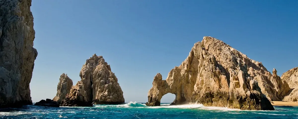 A stunning view of the iconic rock formations at Land's End in Cabo San Lucas, featuring rugged cliffs and a natural arch surrounded by vibrant blue ocean under a clear sky.