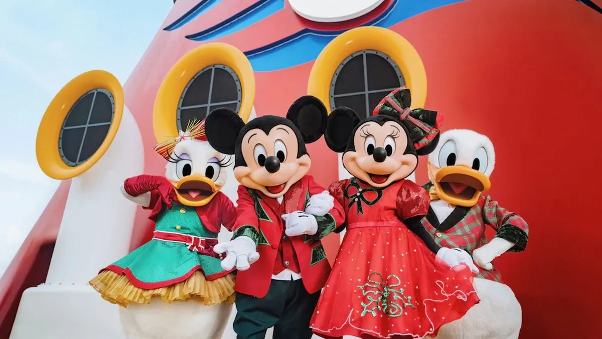 Mickey Mouse, Minnie Mouse, Daisy Duck, and Donald Duck are dressed in festive holiday outfits, standing cheerfully in front of a red and yellow ship funnel with circular windows.