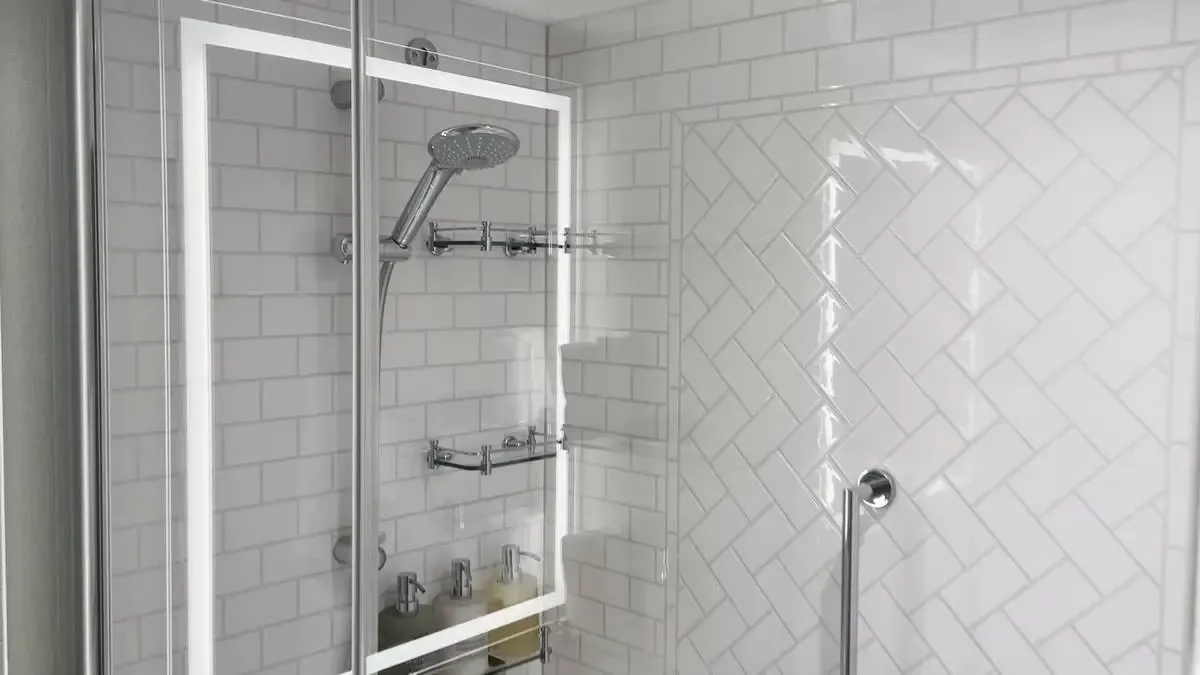 A modern shower with a glass door features a sleek, chrome showerhead and built-in shelves. The walls are covered with white subway tiles arranged in a herringbone pattern, creating a clean and contemporary look.