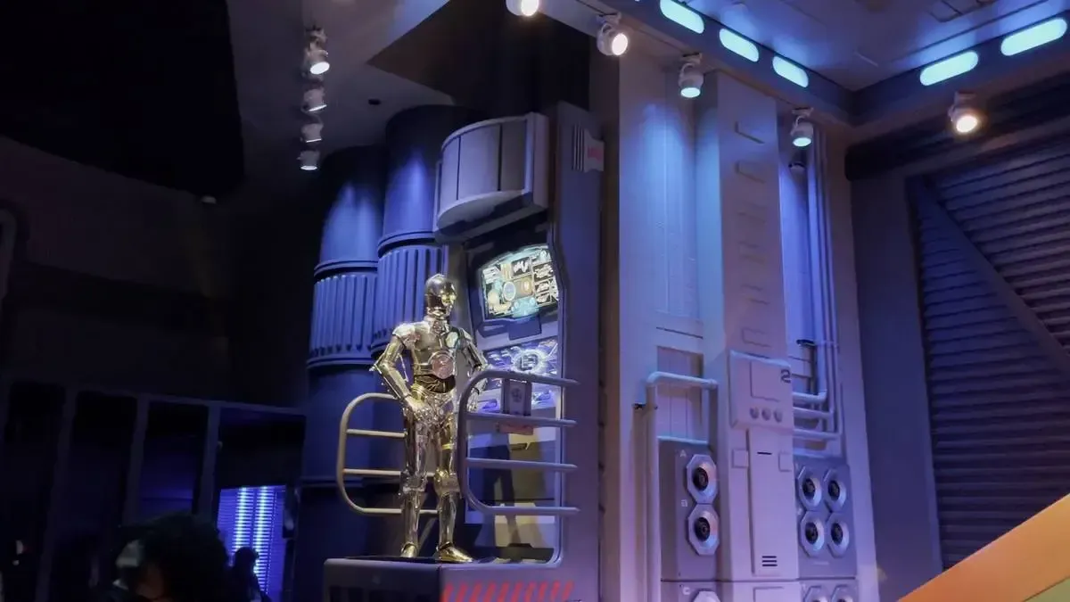 C3PO stands on a platform in a futuristic, dimly lit room with blue and purple lighting, surrounded by high-tech panels and equipment.