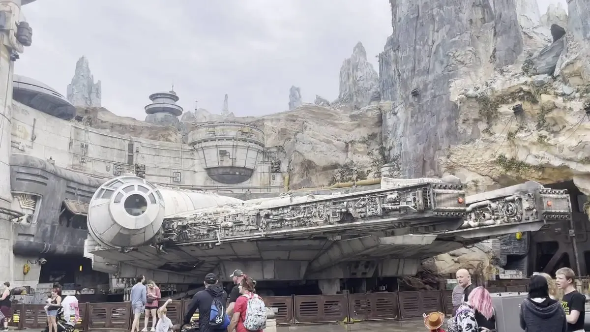 A large, detailed replica of the Millenium Falcon is set against a rocky, sci-fi landscape, with people walking around the area. 