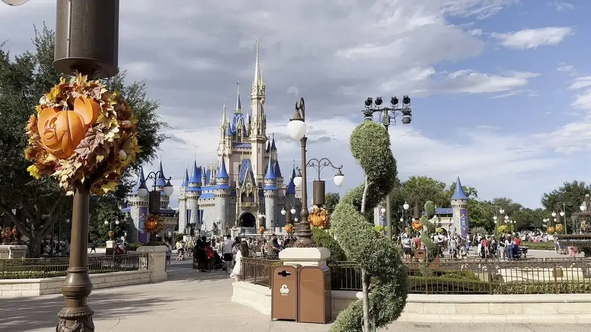 Magic Kingdom castle surrounded by neatly trimmed topiary and festive Halloween decorations, including a pumpkin adorned with leaves on a lamp post.