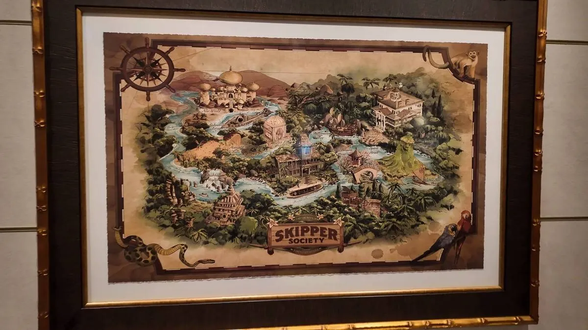 A framed illustrated map titled "Skipper Society" features a whimsical landscape with rivers, lush greenery, and various architectural landmarks, including domed buildings and bridges. Decorative elements like a ship's wheel, a snake, a monkey, and colorful parrots adorn the corners, adding an adventurous theme.