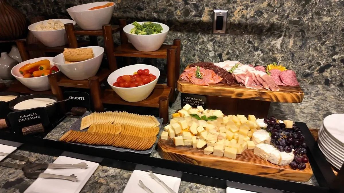 A buffet setup featuring a variety of foods, including a selection of artisanal charcuterie with sliced meats, cubes of cheese, grapes, and crackers.