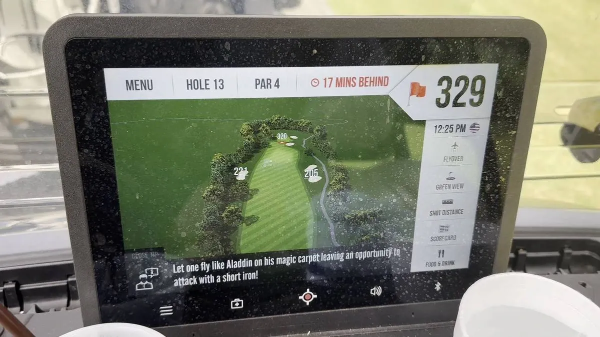 A golf cart screen displays information for golf holes. The screen shows a digital map of the hole with distances marked, and a playful message about "letting one fly like Aladdin".