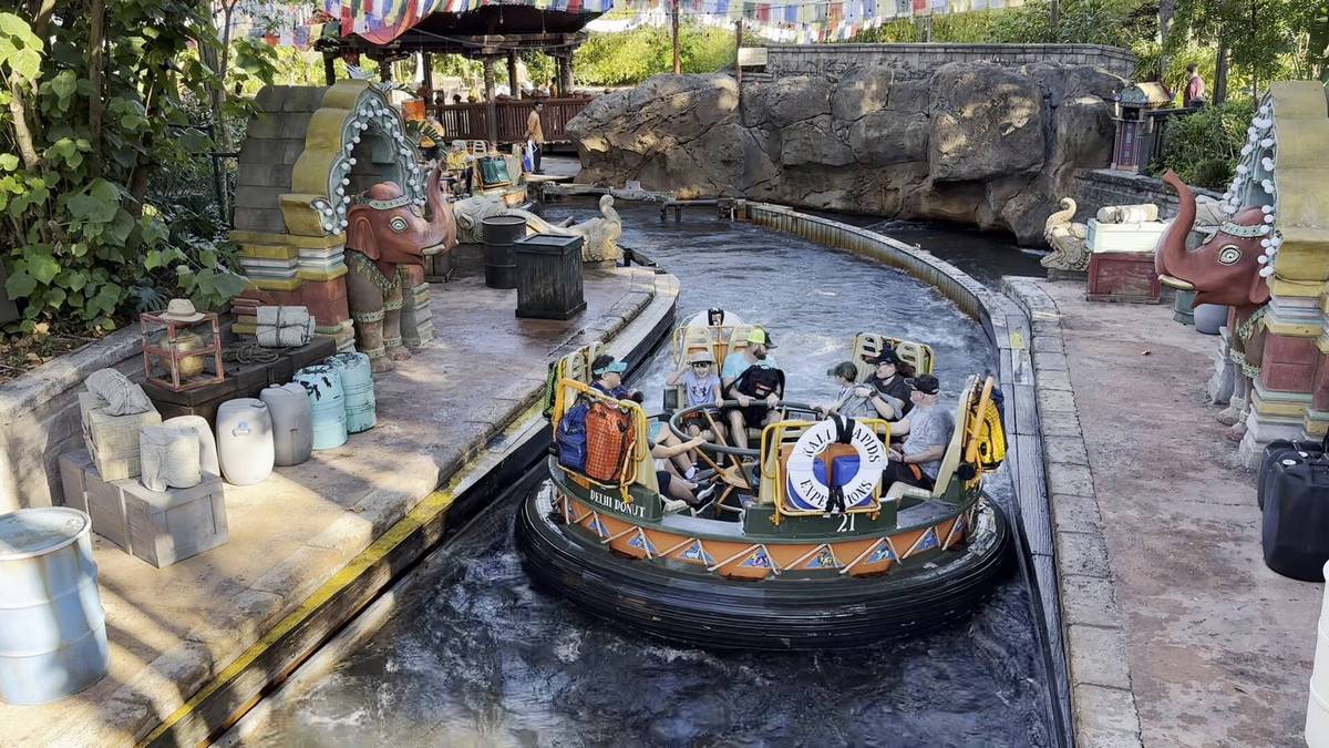 A group of people enjoy a river rapids ride in a circular raft as it navigates through a winding water channel. The setting features colorful statues of elephants and decorative elements along the banks, creating a lively and adventurous atmosphere.