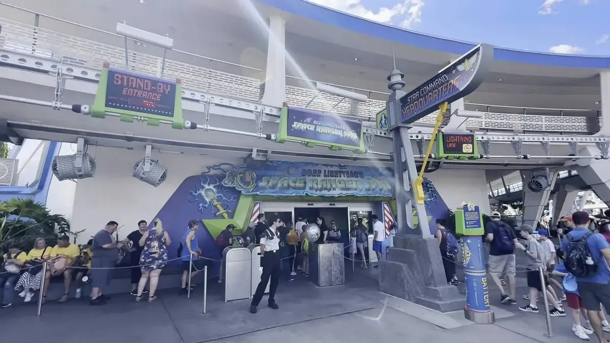 Visitors lining up outside the entrance to Buzz Lightyear's Space Ranger Spin at a theme park, with signs indicating the standby and lightning lane entrances.