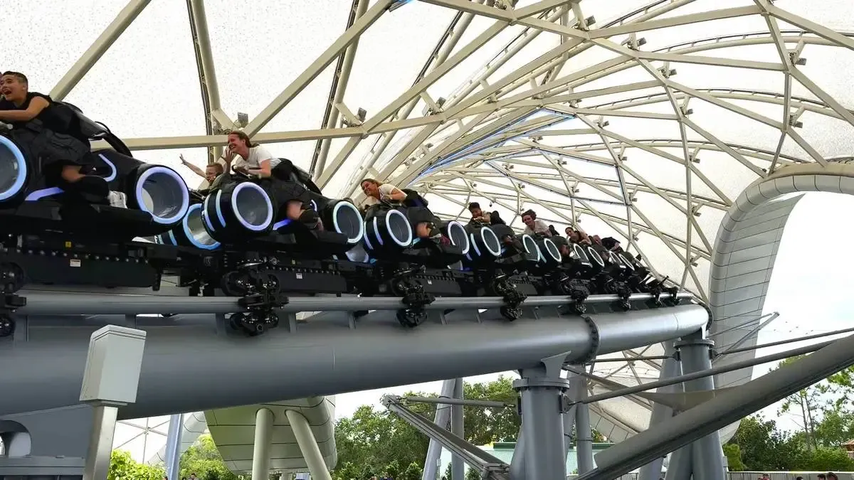 Tron roller coaster with riders on sleek, glowing bikes speeds along a track under a geometric canopy, creating an exciting and dynamic scene.
