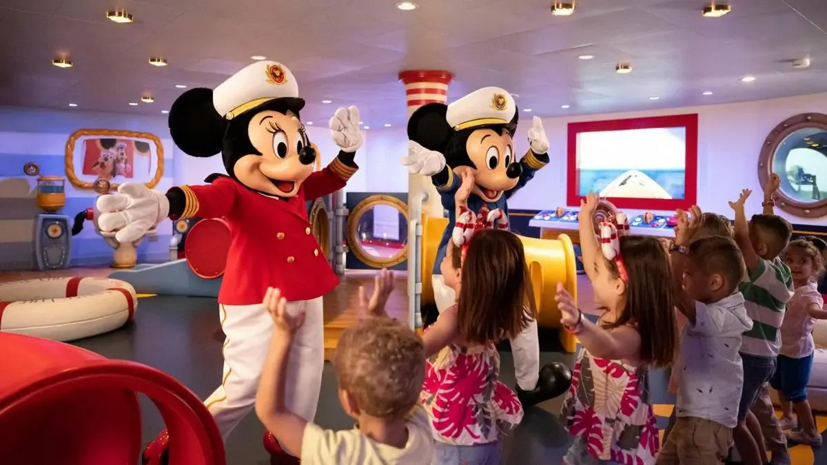 Minnie and Mickey Mouse, dressed in captain uniforms, joyfully greet a group of excited children in a colorful play area, with the kids raising their hands in excitement.