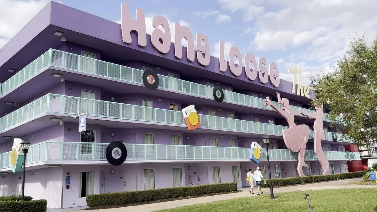 A purple hotel building features large decorative elements, including records and drinks, with bold lettering reading "Hang loose" on the roof. A playful pink silhouette of a dancing figure adorns the facade.