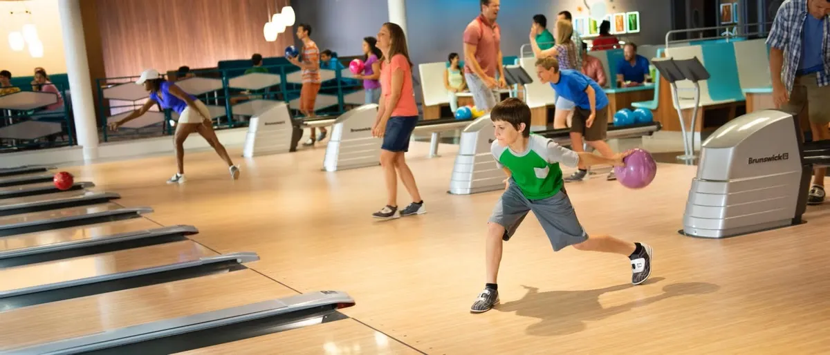A bowling alley scene with several people enjoying the game. There are many people actively engaged in their games. The atmosphere is vibrant, with colorful bowling balls and seating in the background.