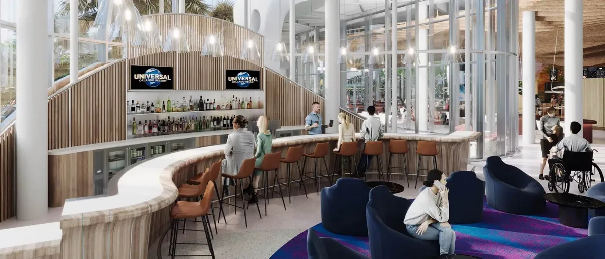 A modern bar area features a curved counter with people seated on orange chairs, enjoying drinks. Behind the bar, shelves are stocked with various bottles, and two screens display the Universal logo.