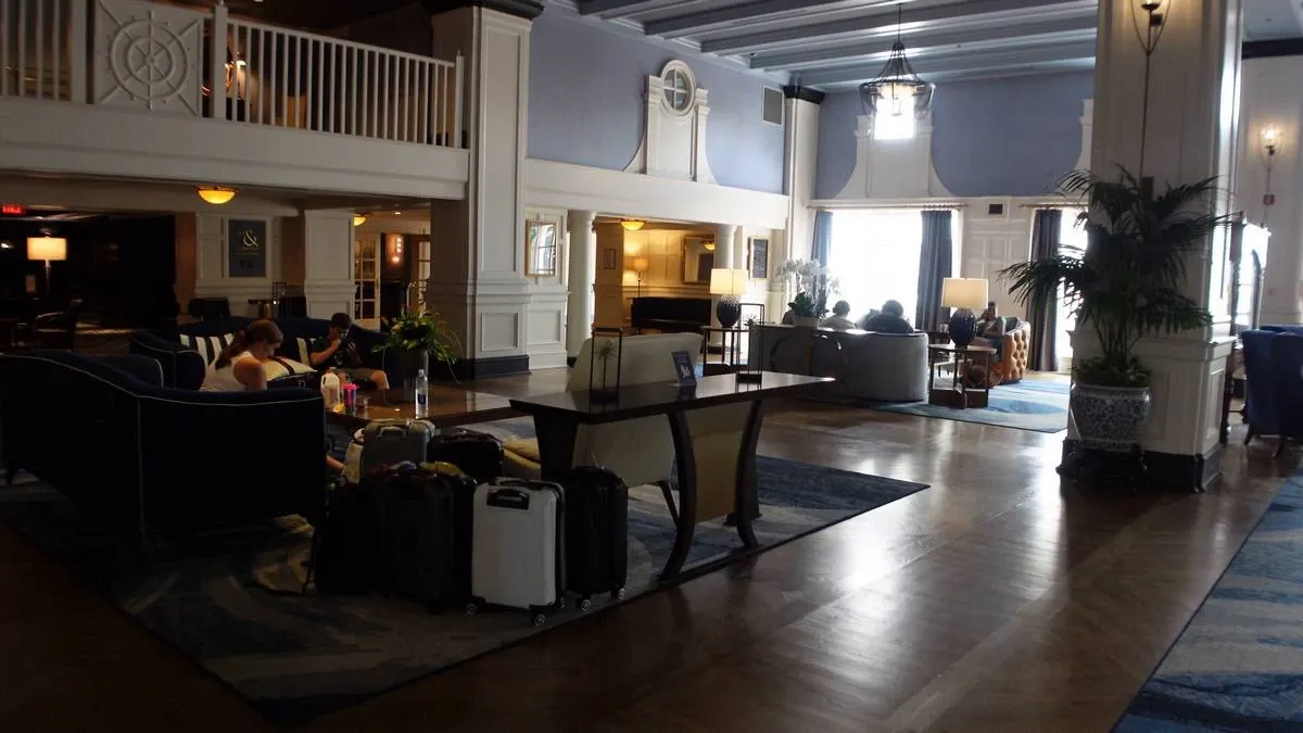 A spacious hotel lobby with elegant decor, featuring a high ceiling and soft lighting. Several people are seated on plush sofas, with luggage placed nearby.
