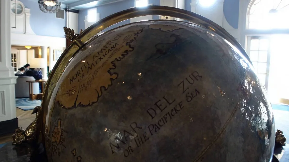 A close-up of an antique globe, features old-fashioned lettering, showing "Mar del Zur or the Pacificke Sea" and "North America or Mexcama." In the background, people are seated on a couch, adding a cozy atmosphere to the setting.